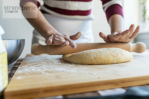 Woman preparing dough with rolling pin to make croissants in kitchen