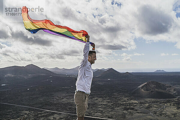 Schwuler junger männlicher Tourist mit einer LGBT-Flagge am Vulkan El Cuervo  Lanzarote  Spanien