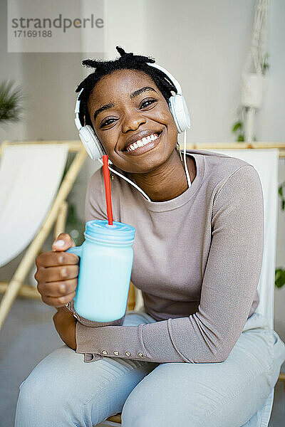 Smiling woman with mason jar sitting on deck chair in living room