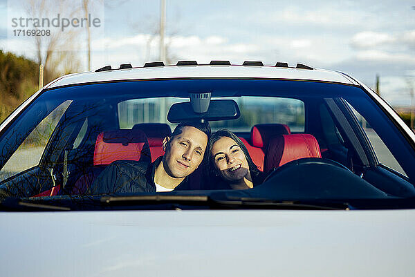 Junges Paar sitzt lächelnd im Auto