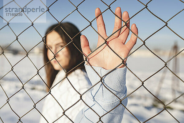 Young woman stretching hand toward fence while standing outdoors