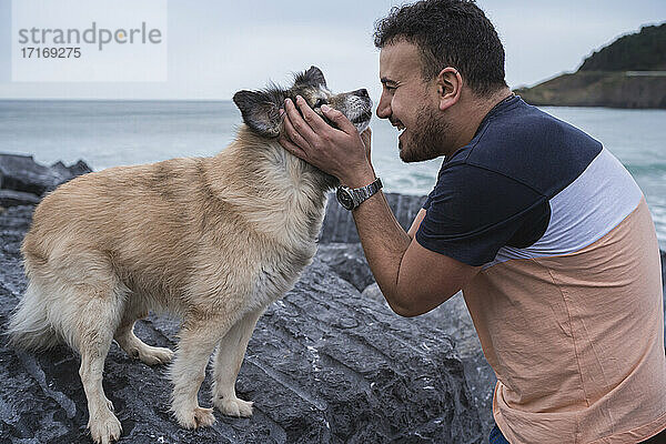 Happy man embracing dog standing on rock formation at beach