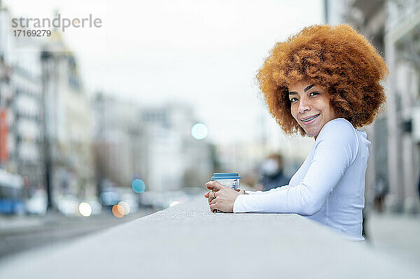 Smiling curly hair woman standing with disposable cup outdoors