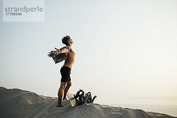 Junger Mann mit ausgestreckten Armen  stehend am Sandbrett in Wüstenshorts in Almeria  Tabernas  Spanien