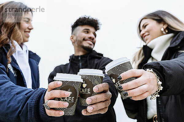 Smiling friend toasting coffee cups while looking at each other