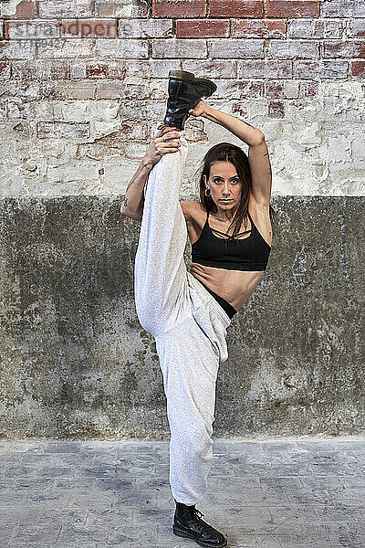 Mid adult female dancer practicing against old brick wall in factory