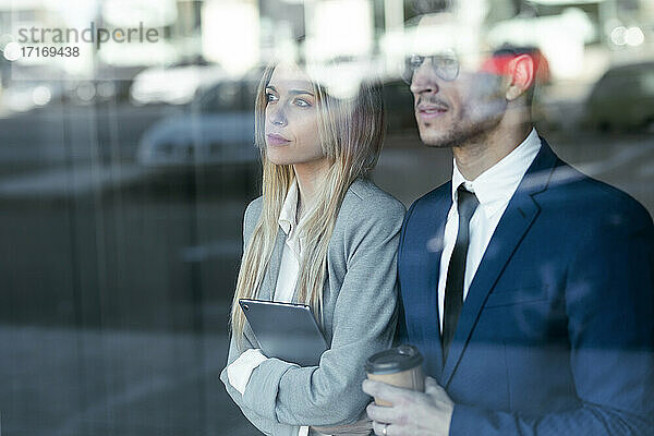Nachdenkliche Geschäftsleute schauen weg  während sie am Bürofenster stehen