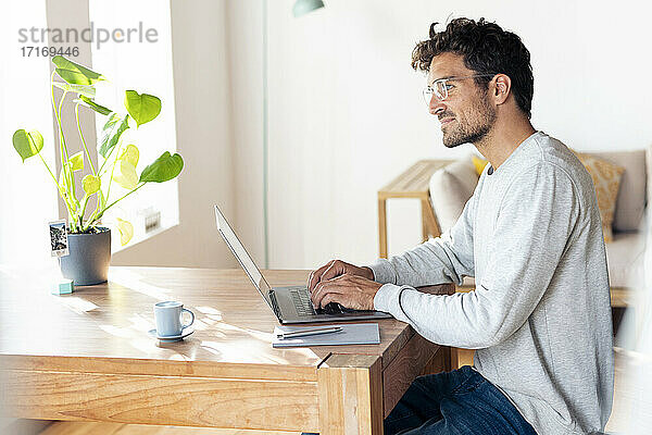 Mann mit Brille  der wegschaut  während er im Büro zu Hause am Laptop sitzt