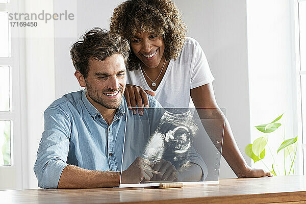 Glückliches Paar prüft Ultraschallbild auf transparentem Bildschirm zu Hause