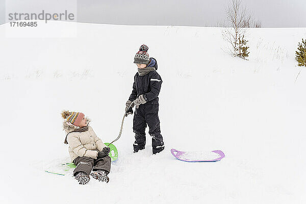 Bruder und Schwester spielen mit einem Schlitten in einer verschneiten Landschaft