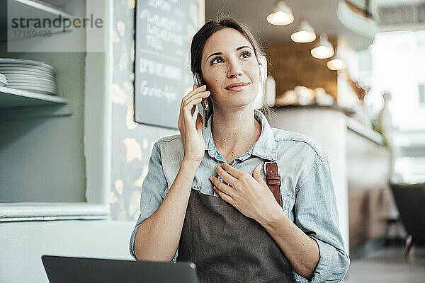 Weiblicher Besitzer  der mit seinem Smartphone telefoniert  während er in einem Café arbeitet