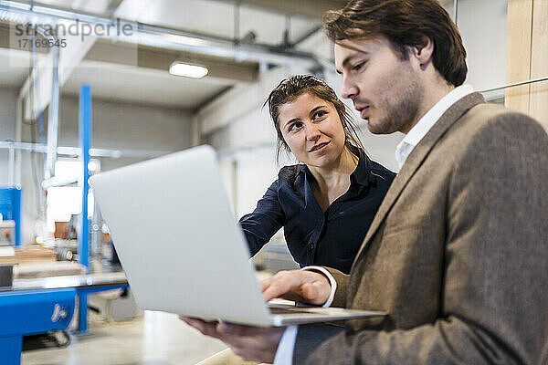 Business people having discussion while working on laptop at industry