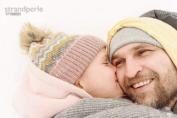 Nahaufnahme einer Tochter  die ihren Vater küsst  während sie im Schnee liegt