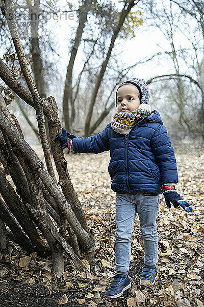 Niedlicher Junge in warmer Kleidung  der im Herbst im Wald steht und wegschaut
