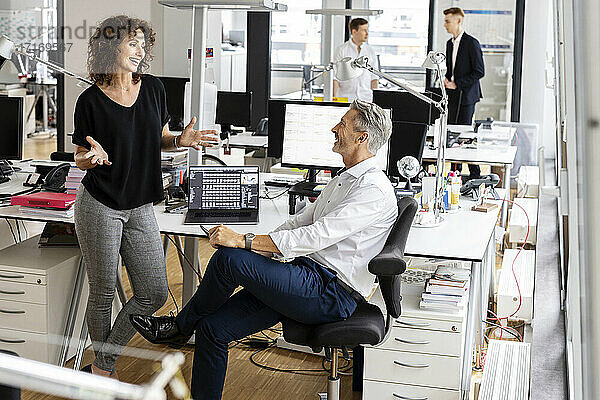 Lächelnde Unternehmer diskutieren  während sie mit Kollegen im Hintergrund in einem Großraumbüro arbeiten