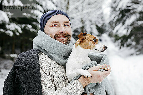 Lächelnder reifer Mann  der im Winter einen Jack Russell Terrier Hund im Schnee trägt