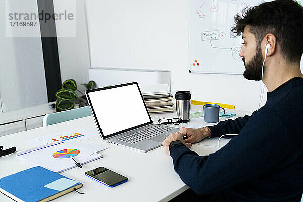 Junger Geschäftsmann schaut auf Laptop in kreativem Büro