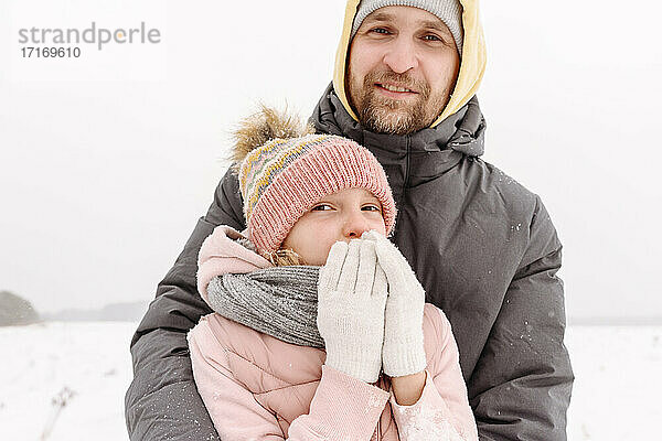 Nahaufnahme eines lächelnden Vaters mit seiner Tochter vor einem klaren Winterhimmel