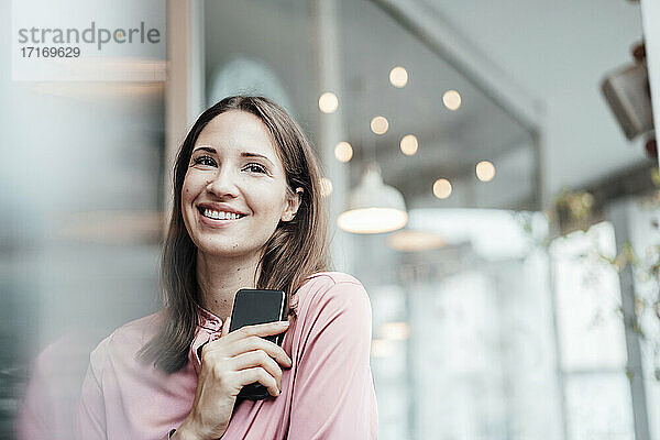 Lächelnde Freiberuflerin  die ihr Smartphone in der Hand hält und im Café wegschaut