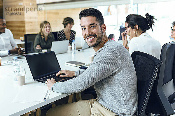 Lächelnder Geschäftsmann  der während einer Sitzung mit Kollegen am Konferenztisch im Sitzungssaal sitzt