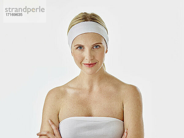 Woman wearing headband and towel staring while standing against white background