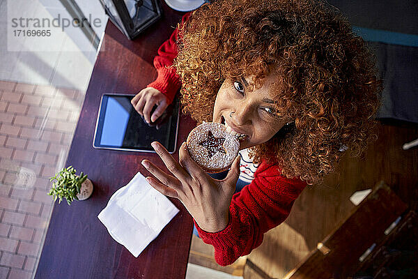 Afro woman eating pancake while sitting at cafe