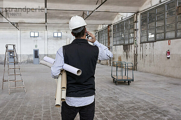 Männlicher Architekt  der Kartons hält und über ein Mobiltelefon spricht  während er in einem Gebäude steht