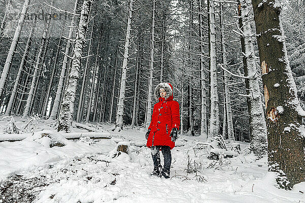 Kleines Mädchen in roter Jacke steht auf schneebedecktem Boden im Wald