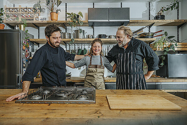 Happy chefs standing with arm around each other in kitchen