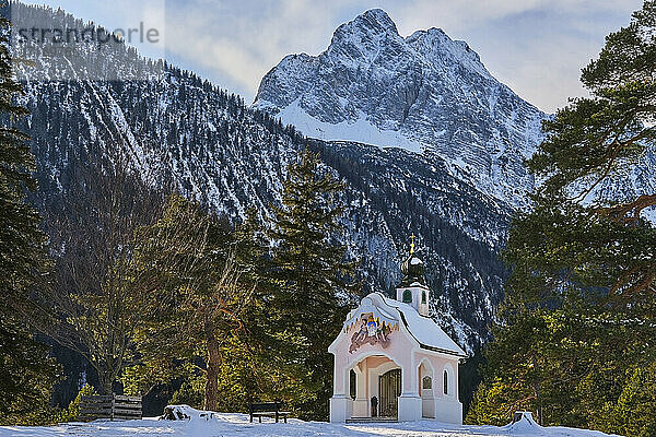 Kapelle am zugefrorenen Seeufer mit schneebedeckten Bergen im Hintergrund  Bayern  Deutschland