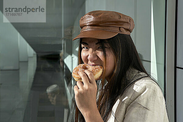 Young woman eating doughnut against glass wall