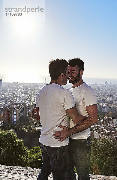 Homosexuelles Paar  das sich umarmt  während es an einem sonnigen Tag vor einer Stadtlandschaft steht  Bunkers del Carmel  Barcelona  Spanien