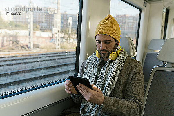 Mittlerer erwachsener Mann in warmer Kleidung  der im Zug sitzend ein digitales Tablet benutzt