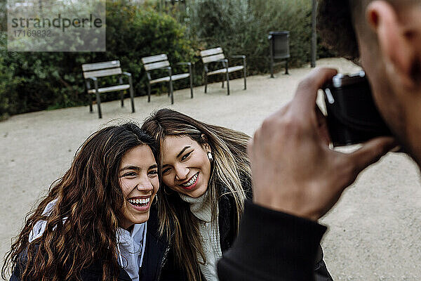 Young man photographing cheerful female friends at park