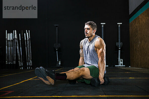 Muskulöser junger Mann mit Hanteln balanciert über den Boden im Fitnessstudio