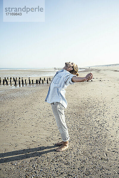 Junger Mann mit ausgestreckten Händen am Strand stehend an einem sonnigen Tag