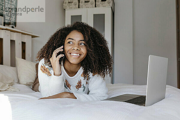 Glückliche Frau  die mit ihrem Handy telefoniert  während sie sich zu Hause auf dem Bett ausruht