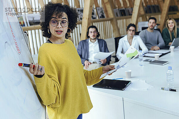 Junge weibliche Hipster-Profis  die auf ein Whiteboard zeigen  während sie ihren Kollegen im Coworking-Büro eine Strategie erklären