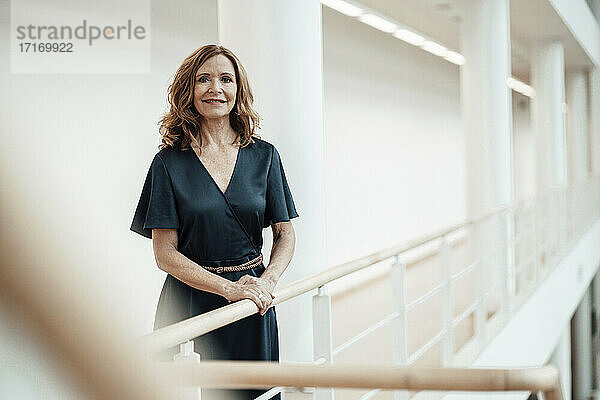 Lächelnde Unternehmerin am Geländer im Korridor