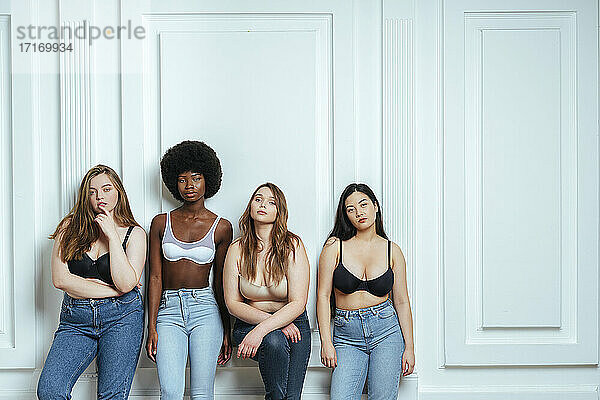 Multi-ethnische Gruppe von Modemodellen  die BHs und Jeans tragen und gegen eine Wand posieren