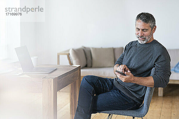 Reifer Geschäftsmann  der ein Mobiltelefon benutzt  während er zu Hause im Büro sitzt