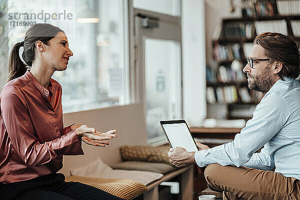 Unternehmerin diskutiert mit einem männlichen Kollegen über ein digitales Tablet in einem Café