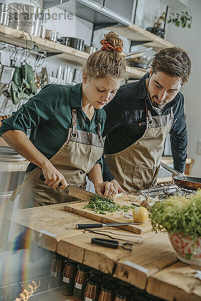 Expertise guiding young colleague to cut scallions while standing in kitchen
