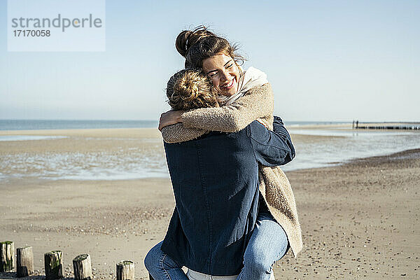 Zärtliches junges Paar umarmt sich am Strand an einem sonnigen Tag