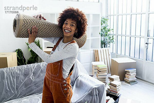 Glückliche Afro-Frau trägt Teppich beim Umzug in ein neues Haus