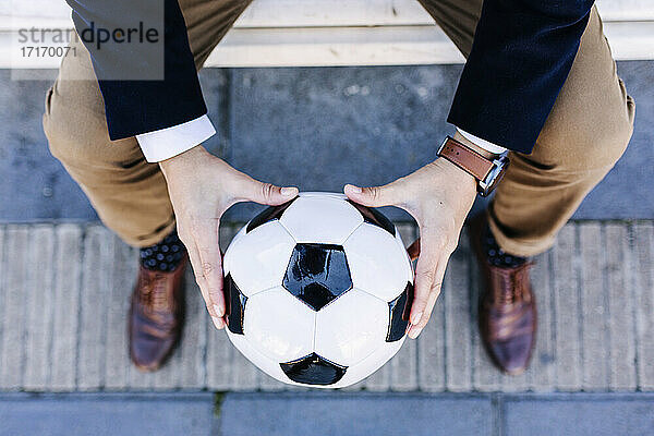 Businessman holding soccer ball while sitting on bench