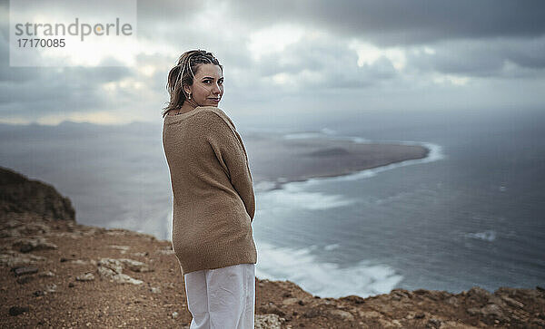 Frau steht auf einem Berg und starrt auf den Strand von Famara  Lanzarote  Spanien