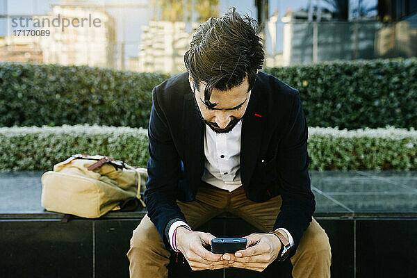 Businessman with bag using mobile phone while sitting on bench