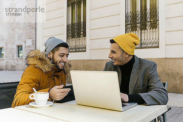 Homosexuell Männer lächelnd bei der Verwendung von digitalen Tablet und Laptop sitzen auf dem Bürgersteig Cafe