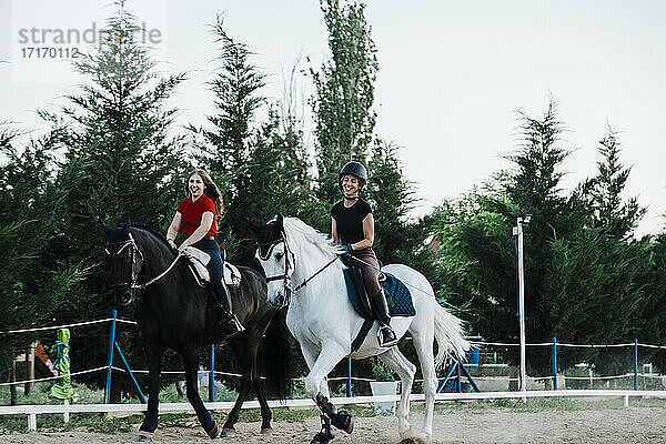 Glückliche Freundinnen reiten auf Pferden in einem Bauernhof